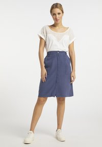 Witte top met geperforeerd patroon, gecombineerd met een knielange marineblauwe rok met een voorste knoop en twee zijzakken. Witte sneakers maken de outfit compleet.