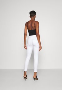 Jeans blancos ajustados con bolsillos traseros, combinados con una camiseta negra ajustada, vistos desde la espalda, con tirantes finos y una textura suave.