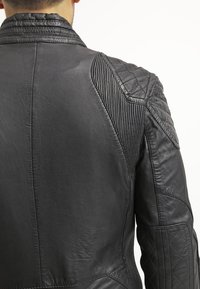 Svart läderjacka med kviltade detaljer på axlar och armar. Har ett texturerat ribbat mönster och en slät yta.