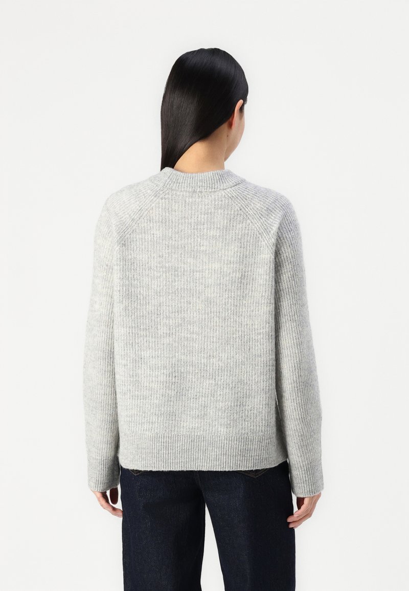 Grau gestrickter Pullover mit gerippter Textur, rundem Halsausschnitt und fallenden Schulternähten, kombiniert mit dunkelblauen Jeans.