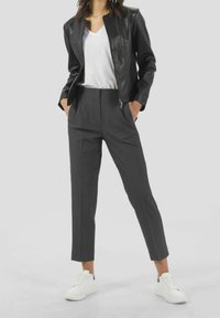 Černá kožená bunda, bílá tričko s výstřihem do V, šedé na míru šité kalhoty a bílé tenisky. Bunda má zapínání na zip a přiléhavý střih.