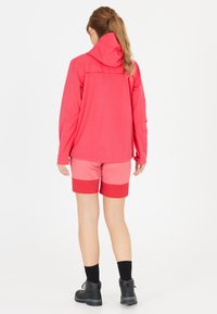 Ljusrosa jacka med huva, i kombination med shorts i rosa och röd färgblock. Svarta ankelskor och svarta strumpor fulländar outfiten.