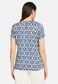 Blouse à manches courtes en tissu léger avec un motif ondulé en bleu marine, bleu clair et crème. Détail de pli au dos pour une coupe décontractée.
