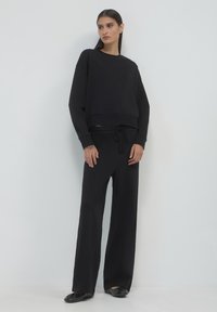 Felpa nera cropped con colllo rotondo e maniche lunghe, abbinata a pantaloni neri larghi con cordino. Texture liscia.
