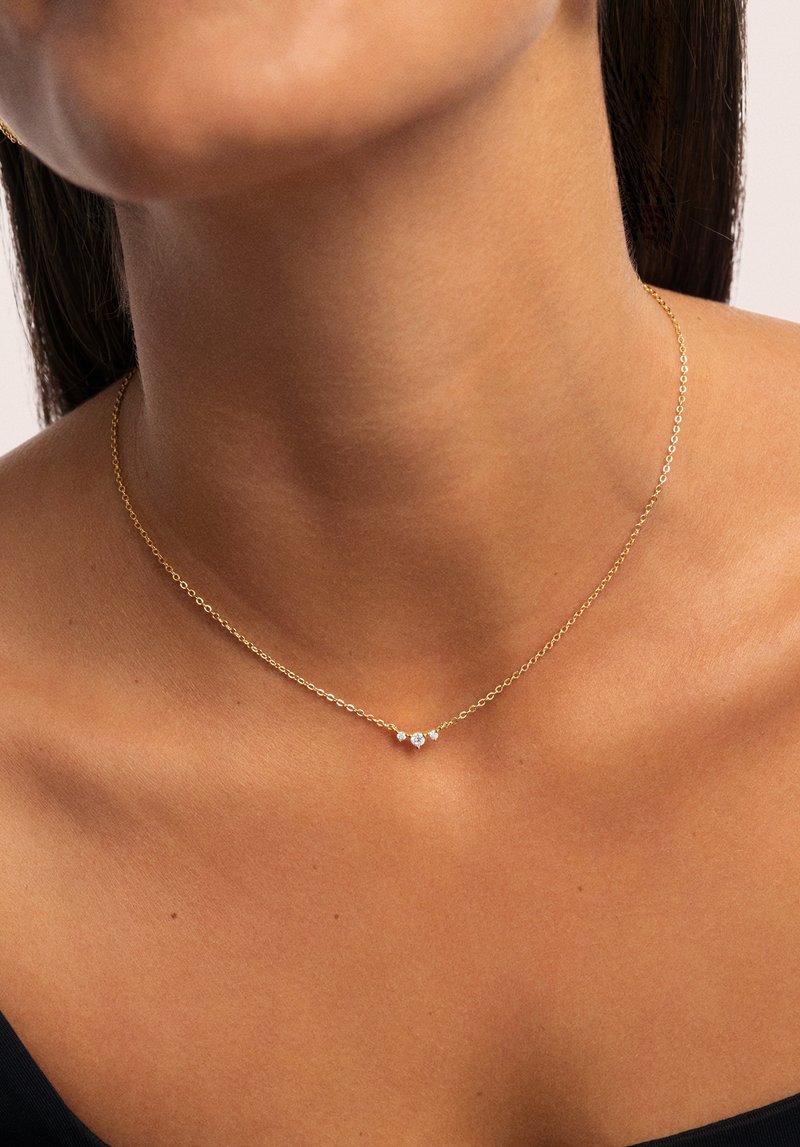 Collana in oro con tre pietre preziose trasparenti al centro. La catena è delicata, con una texture liscia e un design semplice.