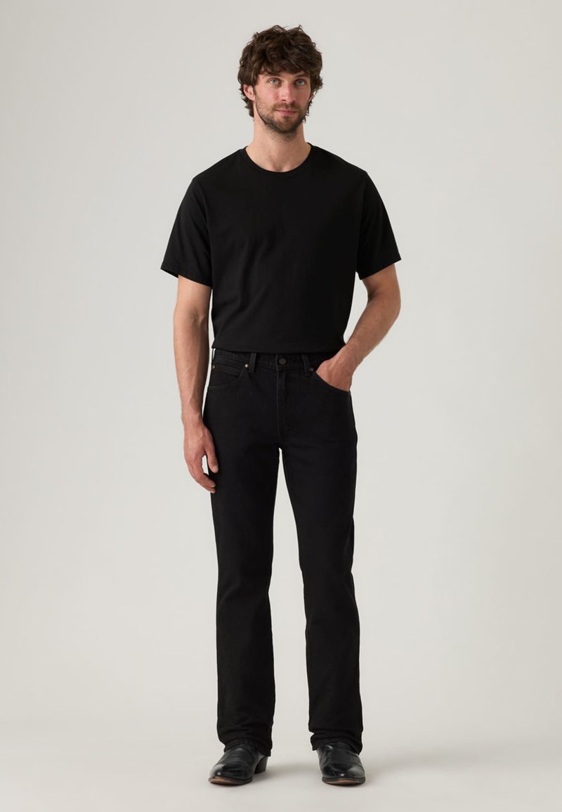 T-shirt in cotone nero abbinata a jeans in denim nero. I jeans hanno una linea a gamba dritta, e le scarpe sono nere con una finitura lucida.