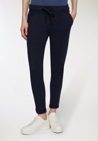 Granatowe joggery z miękkiego materiału, z elastycznym paskiem w talii, regulowanym sznurkiem, bocznymi kieszeniami i podwiniętymi mankietami, w połączeniu z białymi sneakersami.
