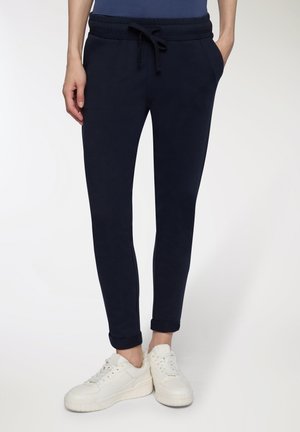 Joggers navy in un tessuto morbido con una vita elastica, cordoncino regolabile, tasche laterali e risvolti, abbinati a sneakers bianche.