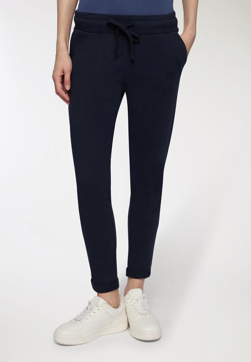 Granatowe joggery z miękkiego materiału, z elastycznym paskiem w talii, regulowanym sznurkiem, bocznymi kieszeniami i podwiniętymi mankietami, w połączeniu z białymi sneakersami.