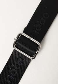 Zwarte geweven band met een zilverkleurige metalen gesp en reliëfbranding. Het materiaal is textuur rijk en duurzaam, met een matte afwerking.