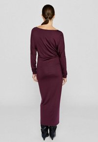 Langärmliges, eng anliegendes, dunkelviolettes Kleid mit einem Bootsauschnitt, aus einem weichen, dehnbaren Material. Glatte Textur, bodenlanges Design.