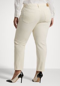 Béžové džíny s rovnými nohavicemi, viditelné zadní kapsy a kožená nášivka. Doplněno černými a béžovými lodičkami na vysokém podpatku.