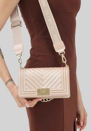 Donna in abito marrone che tiene una borsa a tracolla beige trapuntata con fibbia dorata e tracolla larga con motivo brandizzato.