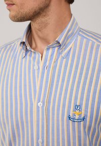 Camicia a righe blu e gialla, realizzata in cotone, con colletto a punta e logo ricamato sul petto.