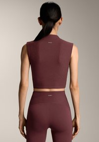 Top corto bordeaux a coste con maniche corte e leggings coordinati a vita alta, con un piccolo logo sulla schiena. Tessuto liscio.