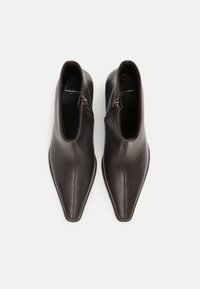 Botas de piel marrón hasta el tobillo con puntera puntiaguda, cremalleras laterales y textura suave. Diseño minimalista sin patrones ni acentos adicionales.