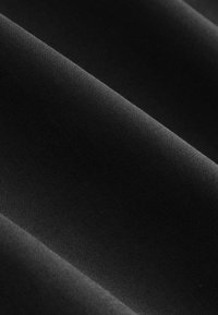 Gros plan d’un tissu noir lisse et étroitement tissé avec des plis subtils créant des ombres douces et une texture.