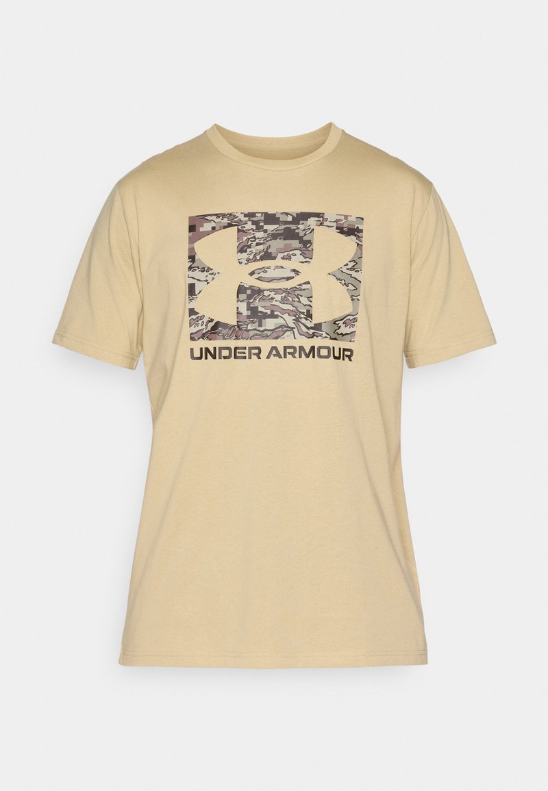 Camiseta de algodón beige de manga corta. Presenta un logo de Under Armour con un patrón de camuflaje y letras oscuras debajo del logo.