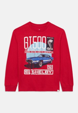 Punane pikkade varrukatega särk, millel on sinise 1969. aasta Shelby GT500 auto graafika, valge tekst ja aktsendid, valmistatud tekstuuriga puuvillamaterjalist.