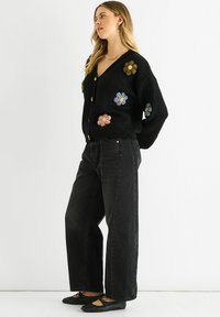 Black knitted cardigan with colorful embroidered flowers, v-neck design, and gold buttons. Paired with high-waisted black jeans and black flats.