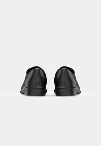 Chaussures en cuir noir avec une texture lisse, bout arrondi et talon bas, présentant des détails de couture subtils à l'arrière.