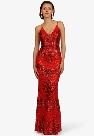 Frau trägt ein bodenlanges rotes Kleid mit glitzernden Blumen- und Diamantmustern, dünnen Trägern und tiefem V-Ausschnitt, stehend vor einem schlichten Hintergrund.