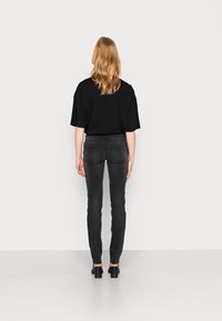 Svart oversized T-shirt och smala svarta jeans, kombinerat med svarta högklackade skor, sedd bakifrån mot en neutral bakgrund.