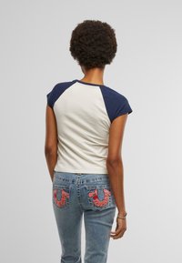 Katoenen cropped t-shirt met marineblauwe raglanmouwen, gecombineerd met blauwe denim jeans met roze geborduurde accenten op de achterzakken.