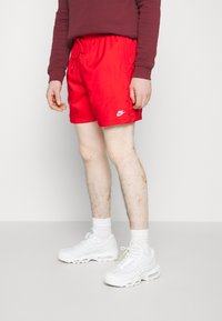 Červené plavecké šortky s elastickým pásom a šnúrkou, so malým bielym logom Nike na boku. V páre s bielymi teniskami.