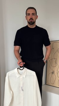 Valge nööpidega särk mustal riidepuul, valmistatud kergest materjalist. Mudel kannab musta lühikeste varrukatega särki, vasakul randmel on kell.