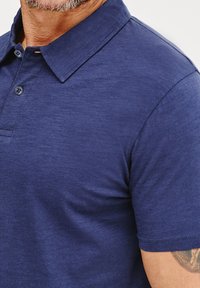Granatowa koszulka polo z teksturowanej tkaniny, z krótkimi rękawami i plakatem na dwa guziki. Charakteryzuje się klasycznym kołnierzykiem i subtelnymi detalami w szyciu.
