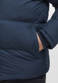 Navy blue puffer jacket with a soft, textured finish. Features a front pocket and ribbed cuffs for added warmth and comfort.