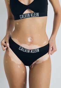 Crni bikini set Calvin Klein s dezénom urezanog gornjeg dijela i logom na donjem dijelu. Glatkova tkanina s mat završetkom.