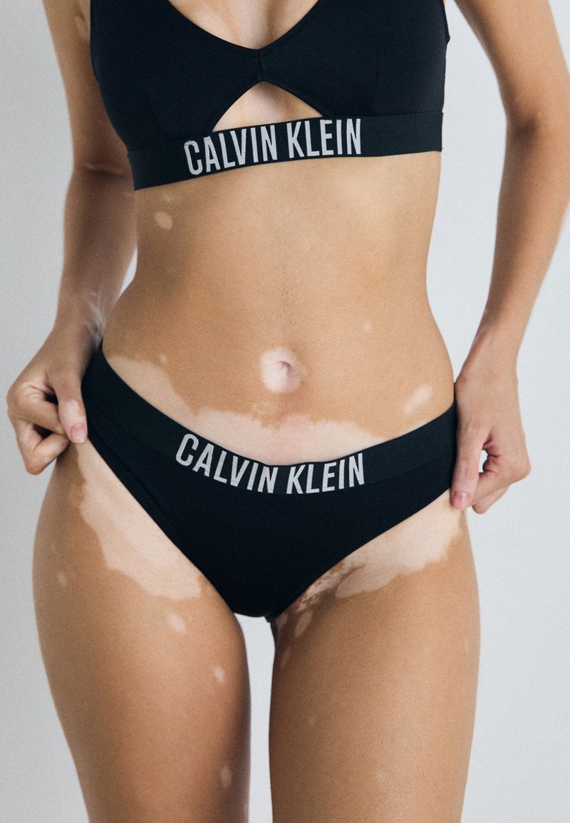 Crni bikini set Calvin Klein s dezénom urezanog gornjeg dijela i logom na donjem dijelu. Glatkova tkanina s mat završetkom.