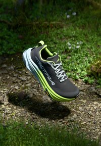 Buty biegowe z ciemnoszarym cholewką, jasnoszarymi akcentami, teksturowaną powierzchnią oraz białą podeszwą środkową z podeszwą Vibram zapewniającą przyczepność.