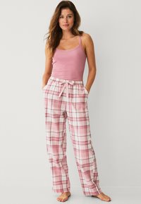 Lichtroze tanktop met kantafwerking, gecombineerd met losse geruite pyjamabroek in tinten van pink en wit, met een elastische tailleband.