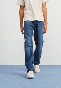 Light blue denim jeans with a straight-leg design, classic five-pocket style, and worn finish. Paired with a light beige t-shirt and white sneakers.