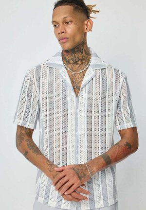 Chemise blanche à manches courtes avec un design en maille tissée et des rayures verticales. Présente un col camp et une coupe décontractée.