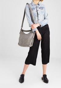 Grijze nep leren schoudertas met een slouchy ontwerp, brede schouderband en subtiele textuur, gecombineerd met zwarte plooibroek en spijkerjas.