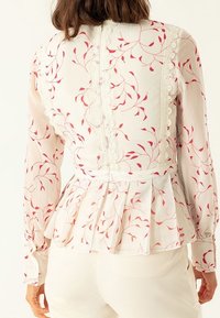 Blusa a maniche lunghe in tessuto rosa chiaro con motivo floreale rosso, caratterizzata da un bordo in pizzo e un orlo a peplo, con chiusure a bottone sul retro.
