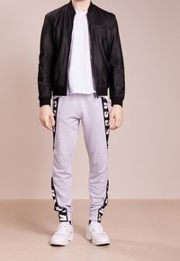 Svart bomberjacka över en vit t-shirt, kombinerad med grå sweatpants som har sidostrikar. Vita sneakers fulländar outfiten.