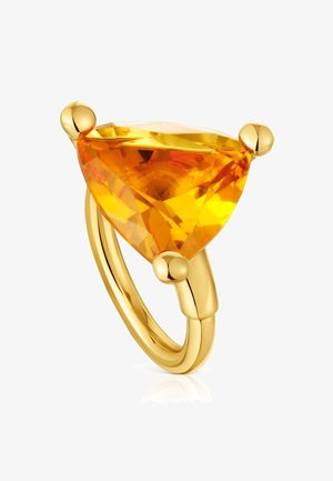 Anillo de oro con una gran piedra preciosa naranja de corte triangular sostenida por tres garras de oro sobre un fondo blanco.
