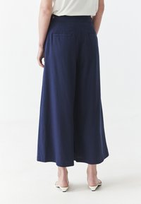 Pantalones de pierna ancha en color navy, confeccionados en lino, con cintura alta, bolsillos laterales y detalle de botón en la parte trasera. Textura suave y ajuste cómodo.