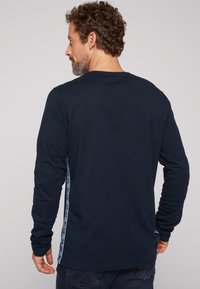 Camicia a maniche lunghe blu navy in morbido cotone, con un pannello laterale su cui è stampato in azzurro chiaro "BLUE 2501" lungo la cucitura.