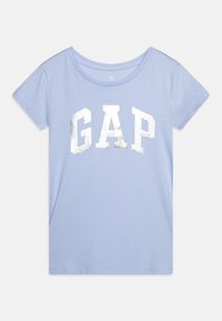 Šviesiai mėlyna trumpomis rankovėmis marškinėliai su apvaliu kaklu, ant kurių priekyje išdidžiai pavaizduotas didelis sidabrinis metalinis "GAP" logotipas.