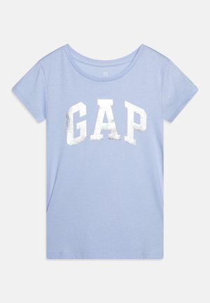 Šviesiai mėlyna trumpomis rankovėmis marškinėliai su apvaliu kaklu, ant kurių priekyje išdidžiai pavaizduotas didelis sidabrinis metalinis "GAP" logotipas.
