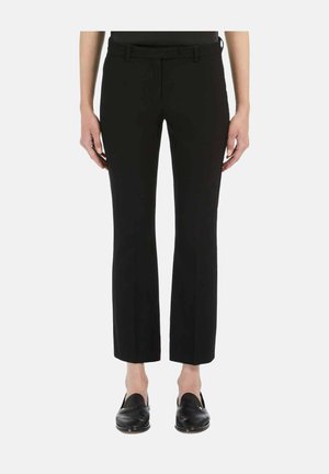 Zwarte broek met rechte pijpen, voorzakken en riemlussen, gedragen met zwarte instapschoenen door een persoon die voor een witte achtergrond staat.