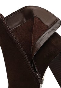 Bruine suede enkellaars met leren afwerking en rits sluiting. De hak heeft een textuur met een contrasterend patroon. Zachte binnenvoering.