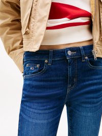 Donkerblauwe denim jeans met een slim fit, voorzien van voorzakken en metalen hardware. Gdraagd met een beige bomberjack en een gestreept trui.