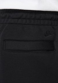 Melnas sporta bikses ar gludu tekstūru, ar elastīgu jostu un mazu melnu Nike logo. Iekļauj aizmugurējo kabatu.